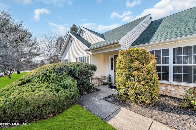 view of exterior entry with stone siding and roof with shingles