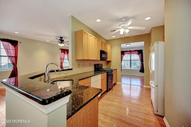 kitchen with light wood-style floors, light brown cabinets, a sink, a peninsula, and black appliances