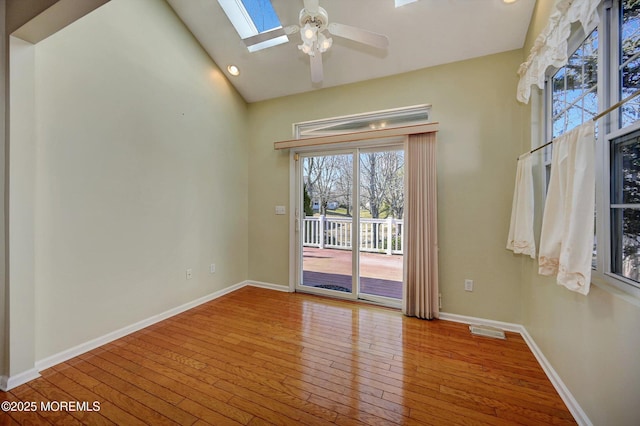 spare room featuring hardwood / wood-style flooring, vaulted ceiling with skylight, visible vents, and baseboards