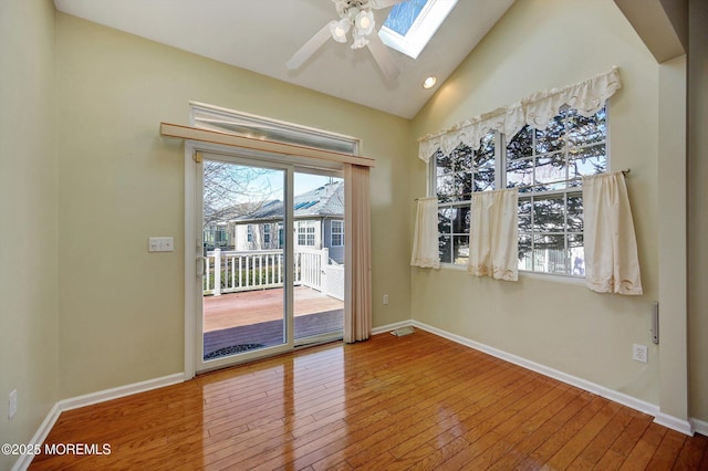 interior space featuring lofted ceiling with skylight, baseboards, and hardwood / wood-style floors