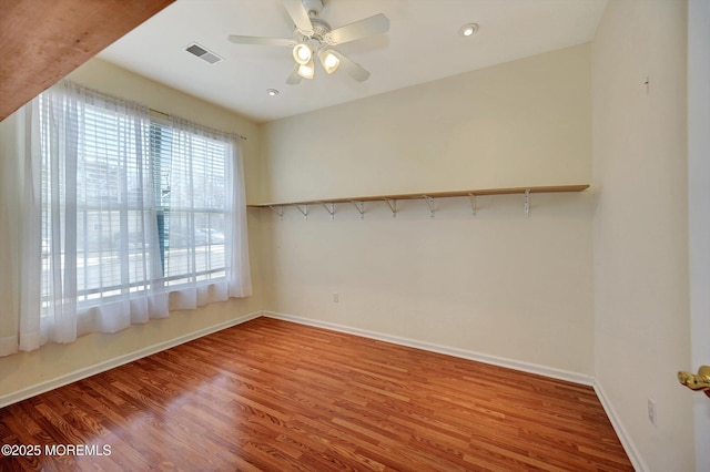 unfurnished room featuring a ceiling fan, wood finished floors, visible vents, and baseboards