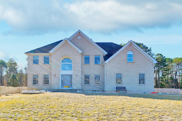 view of front facade featuring brick siding, fence, and a front lawn