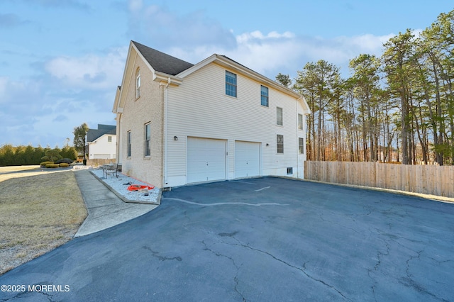 view of side of property featuring driveway, an attached garage, and fence