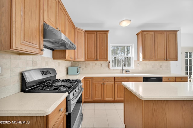 kitchen with light countertops, light tile patterned flooring, a sink, under cabinet range hood, and stainless steel gas range oven