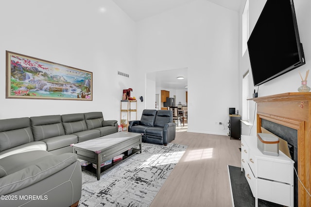 living room featuring visible vents, a fireplace, a high ceiling, and wood finished floors