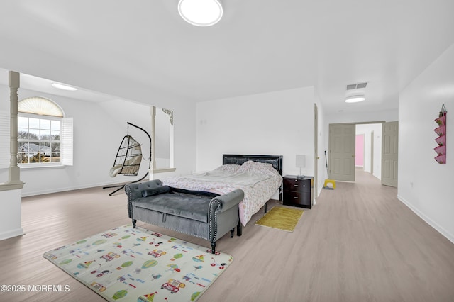 bedroom with light wood finished floors, decorative columns, visible vents, and baseboards