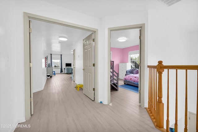 hallway with a wealth of natural light, visible vents, and light wood-style flooring