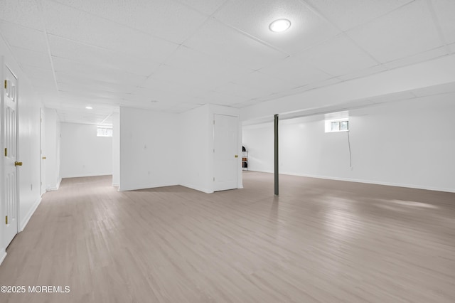 basement with plenty of natural light, a drop ceiling, light wood-type flooring, and baseboards