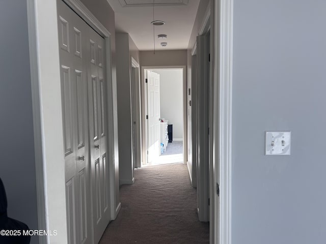 hallway with attic access, dark carpet, and baseboards