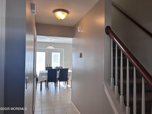 hallway featuring light tile patterned flooring, baseboards, and stairs