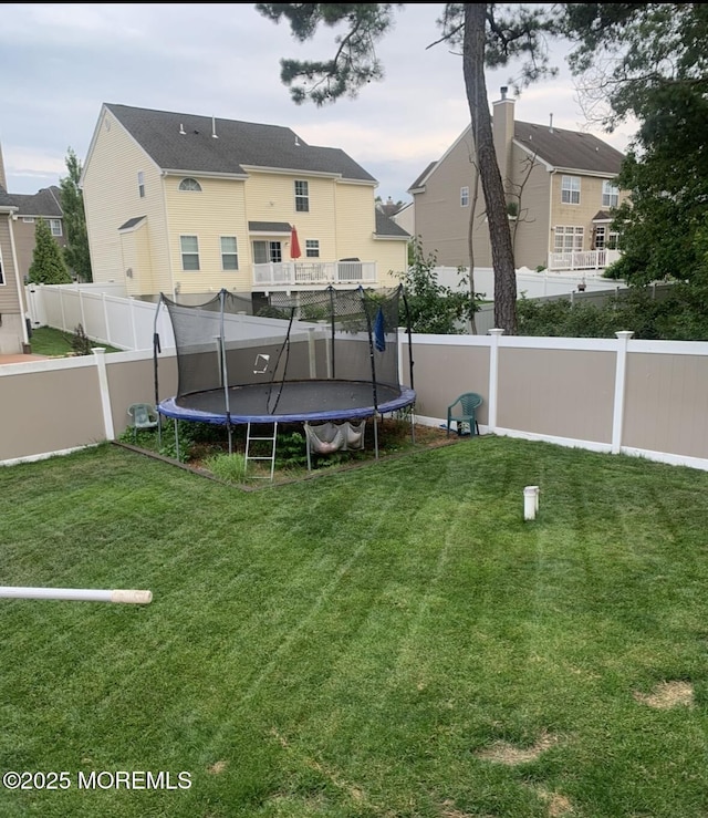 rear view of house featuring a trampoline, a fenced backyard, and a lawn