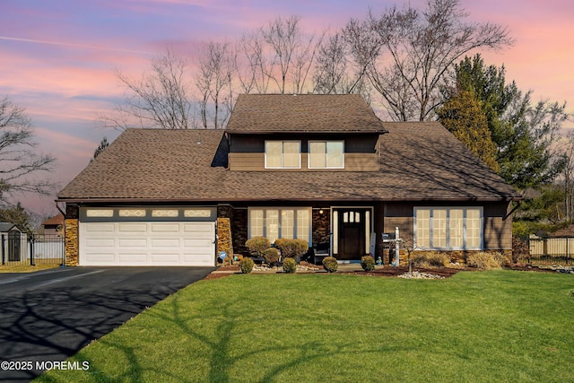 view of front of home with aphalt driveway, stone siding, fence, a yard, and an attached garage