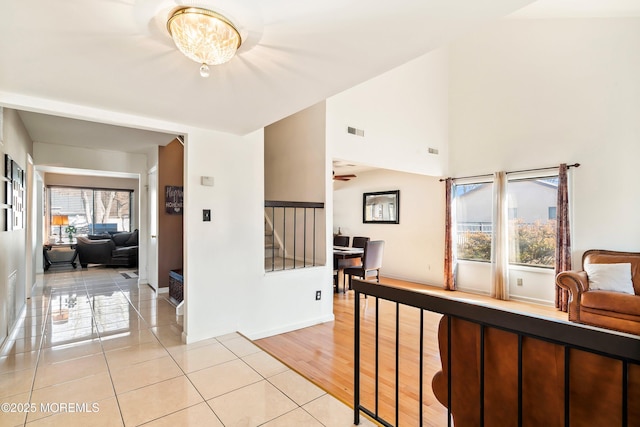 corridor featuring visible vents, baseboards, a high ceiling, and light tile patterned flooring