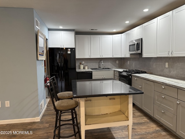 kitchen featuring black appliances, a breakfast bar area, a sink, and dark wood finished floors