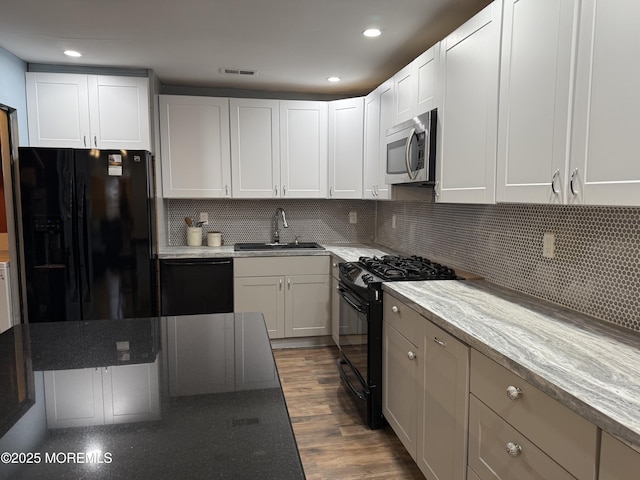 kitchen with dark wood-type flooring, a sink, visible vents, black appliances, and tasteful backsplash