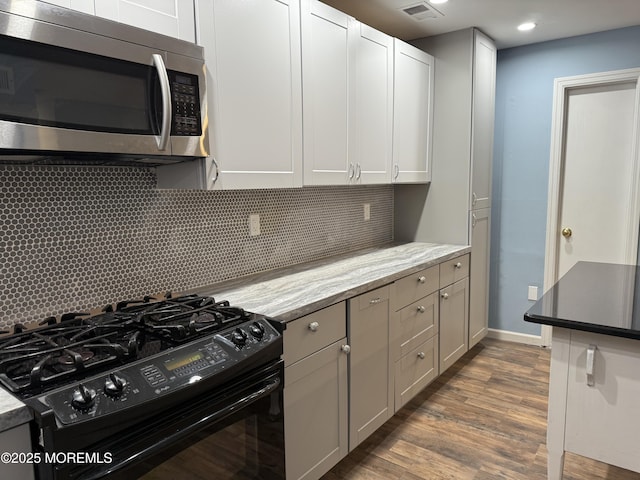 kitchen with dark wood-style flooring, light stone countertops, tasteful backsplash, stainless steel microwave, and black gas range oven