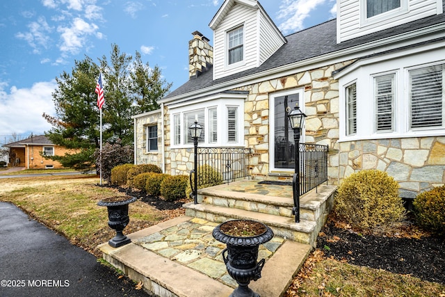 view of exterior entry featuring stone siding and a chimney