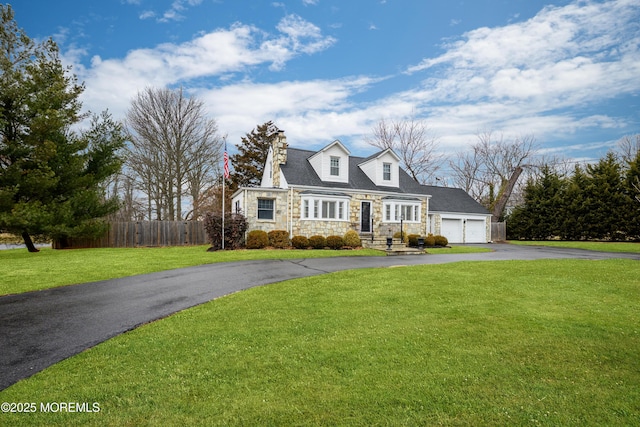 cape cod-style house featuring aphalt driveway, an attached garage, fence, stone siding, and a front yard