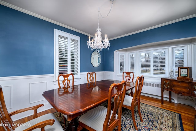 dining room with an inviting chandelier, crown molding, wood finished floors, and wainscoting