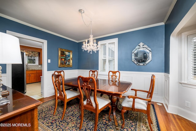 dining area with light wood finished floors, crown molding, and wainscoting
