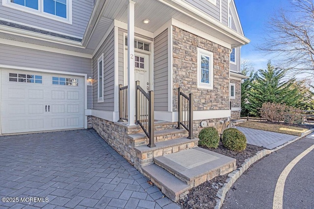 entrance to property featuring a garage, decorative driveway, and stone siding