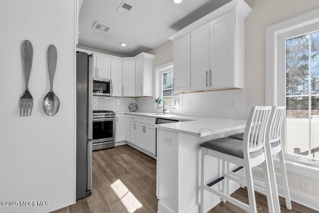 kitchen featuring stainless steel appliances, dark wood-type flooring, a peninsula, and visible vents