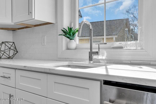 kitchen featuring tasteful backsplash, white cabinets, stainless steel dishwasher, and light stone countertops