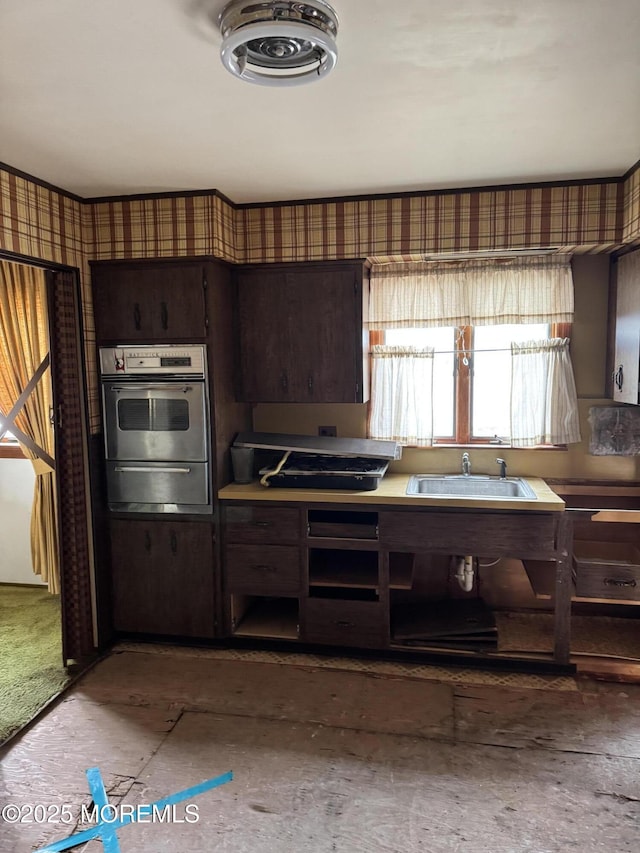 kitchen featuring oven, dark brown cabinetry, a sink, a warming drawer, and wallpapered walls