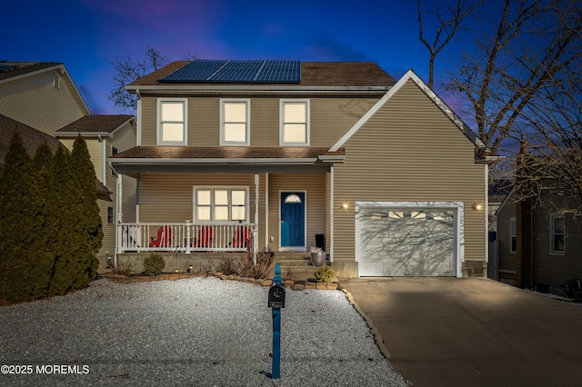 traditional-style house with a porch, a garage, driveway, roof with shingles, and roof mounted solar panels