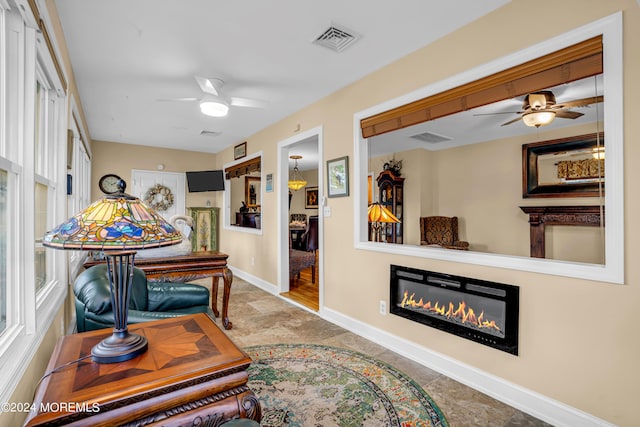 office space featuring ceiling fan, a glass covered fireplace, visible vents, and baseboards