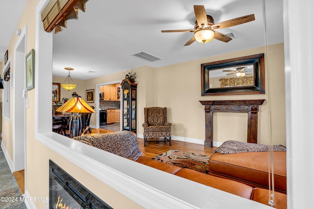 living room featuring a warm lit fireplace, baseboards, visible vents, and wood finished floors