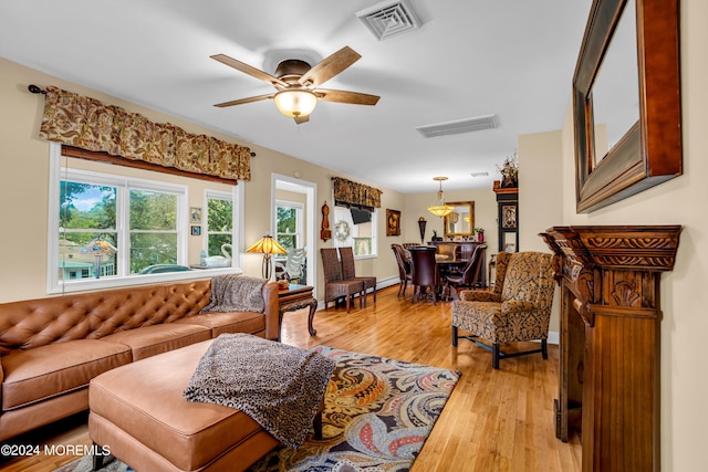 living room featuring baseboards, light wood finished floors, visible vents, and a ceiling fan