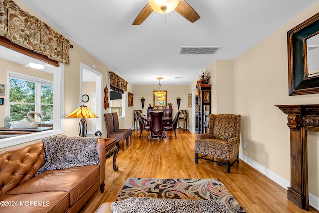 living area featuring a ceiling fan, light wood-type flooring, visible vents, and baseboards