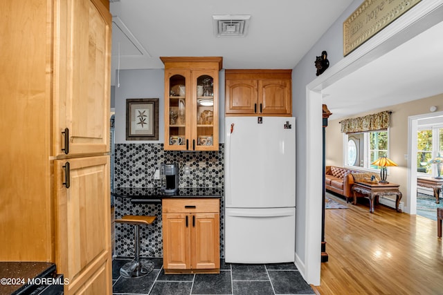 kitchen featuring tasteful backsplash, dark countertops, visible vents, glass insert cabinets, and freestanding refrigerator