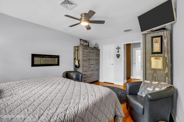 bedroom with a ceiling fan, visible vents, baseboards, and wood finished floors