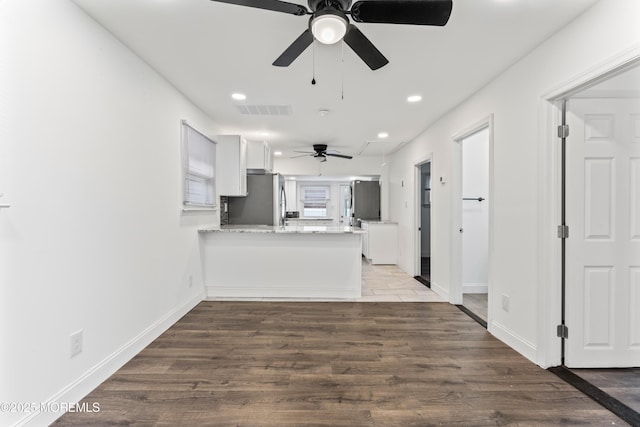 kitchen featuring visible vents, wood finished floors, freestanding refrigerator, a peninsula, and white cabinetry