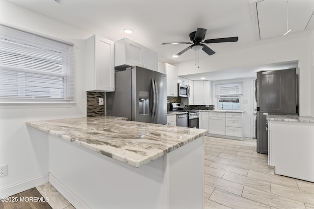 kitchen with stainless steel appliances, tasteful backsplash, a peninsula, and white cabinetry