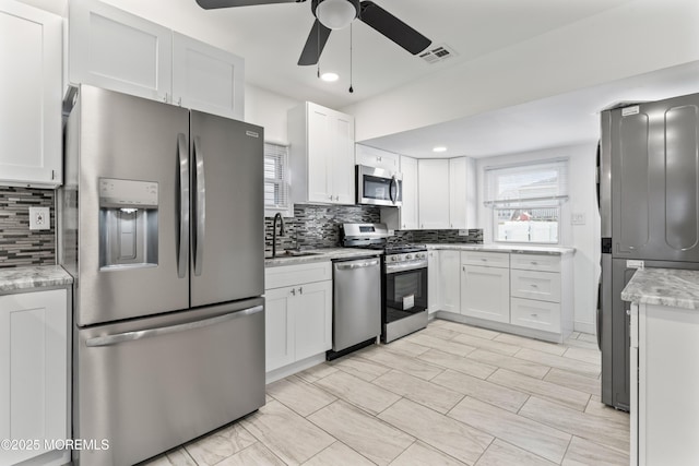 kitchen with stainless steel appliances, a sink, visible vents, white cabinetry, and decorative backsplash