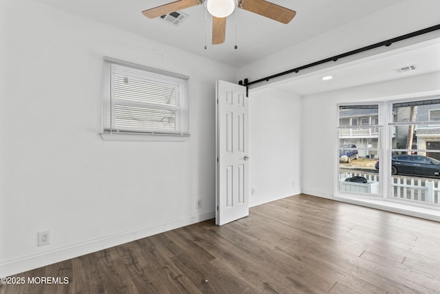 spare room featuring visible vents, a barn door, ceiling fan, wood finished floors, and baseboards