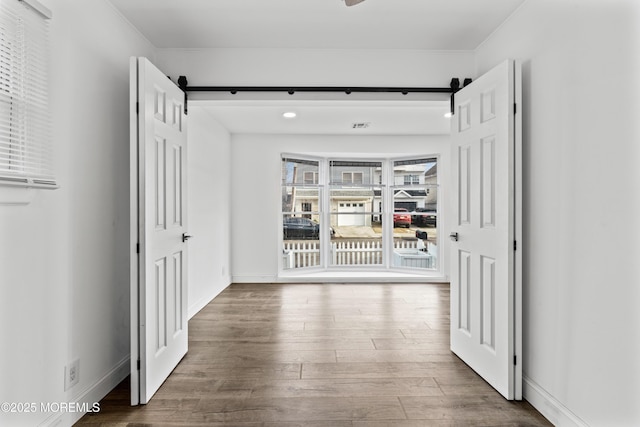 hall featuring a barn door, baseboards, and wood finished floors