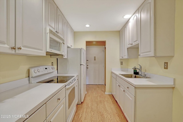 kitchen featuring light countertops, white cabinets, a sink, light wood-type flooring, and white appliances