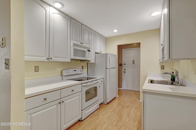 kitchen with white appliances, light wood-style flooring, light countertops, a sink, and recessed lighting