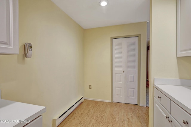 kitchen with white cabinets, light wood-type flooring, baseboard heating, and light countertops