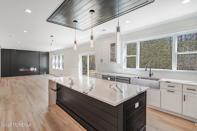 kitchen with ornamental molding, white cabinetry, a sink, and light stone counters