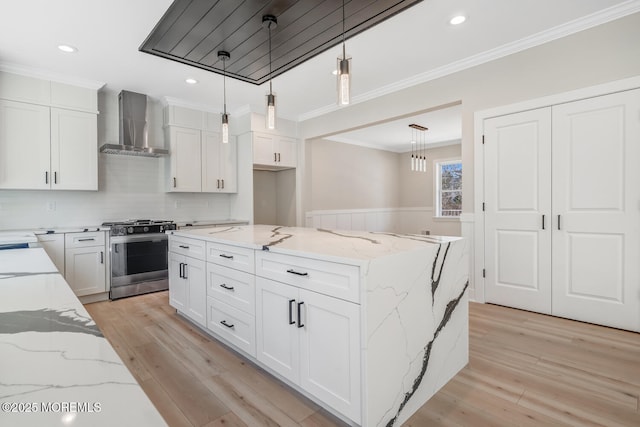 kitchen with ornamental molding, wall chimney range hood, stainless steel gas range, and light wood-type flooring