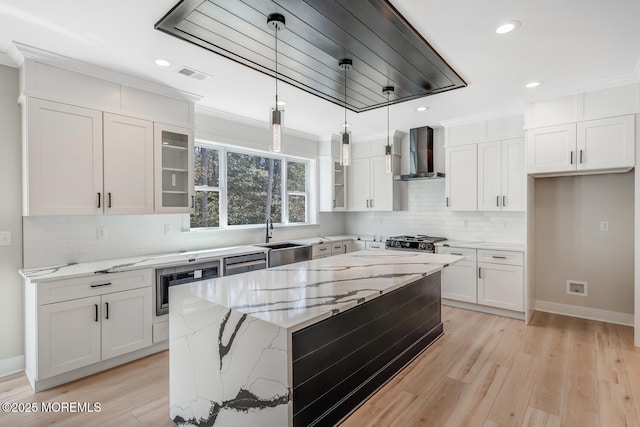 kitchen with visible vents, stove, white cabinetry, a sink, and wall chimney exhaust hood