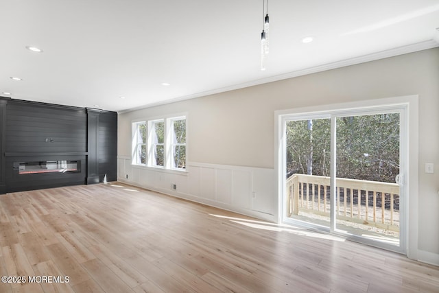 unfurnished living room featuring a large fireplace, light wood-style floors, and a wainscoted wall