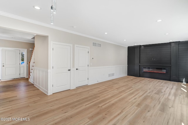 unfurnished living room with a wainscoted wall, light wood-style flooring, stairway, and visible vents