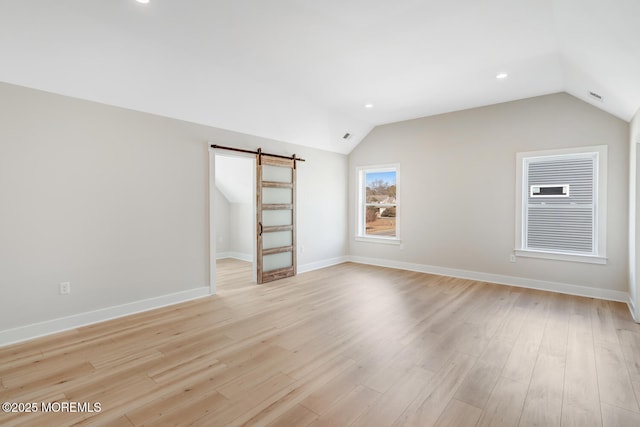 unfurnished room featuring vaulted ceiling, a barn door, light wood-style flooring, and baseboards