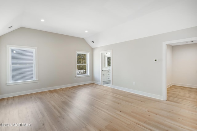 spare room with lofted ceiling, baseboards, and light wood-style floors